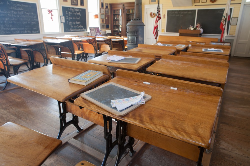 An old, empty school room with desks and chairs.